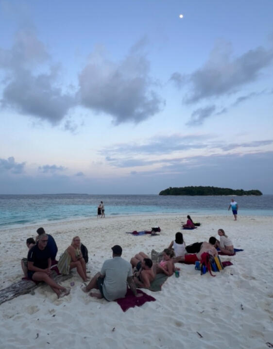 Kleine Reisegruppe sitzt bei Dämmerung gemeinsam auf einer Sandbank